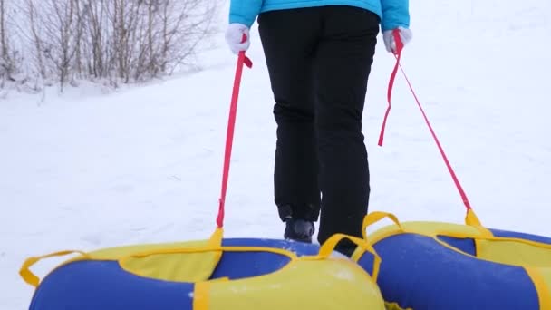 女性は、凍るような冬の日に雪の受け皿を手に持った高雪の山に登っていきます。女の子は、そりの手のキャリーです。クリスマス — ストック動画