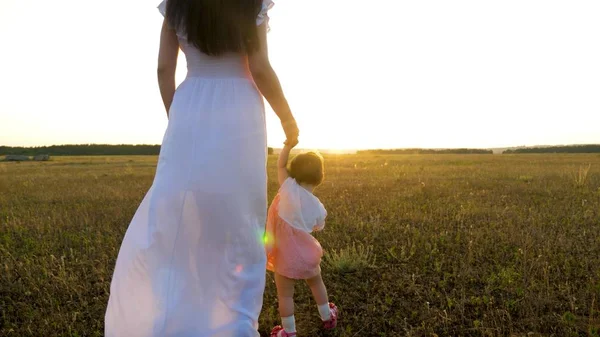 Pequeño bebé va adelante sosteniendo su mano madre en la puesta del sol brillante —  Fotos de Stock