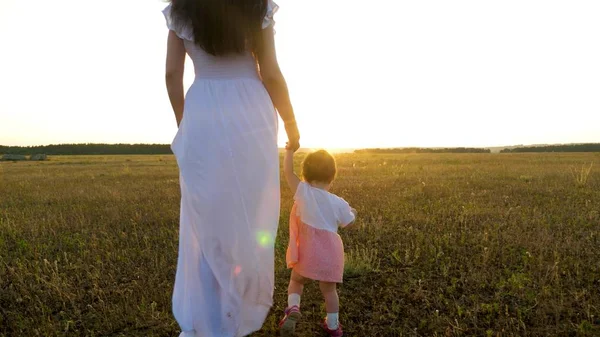 Kleine baby gaat vooruit bezit is van de hand van zijn moeder in heldere zonsondergang — Stockfoto