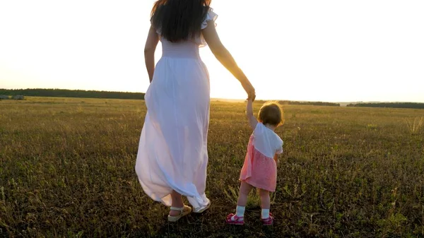 Pequeno bebê vai para a frente segurando sua mãe mão no pôr do sol brilhante — Fotografia de Stock