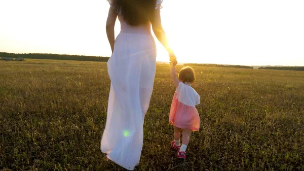 Pequeno bebê vai para a frente segurando sua mãe mão no pôr do sol brilhante — Fotografia de Stock