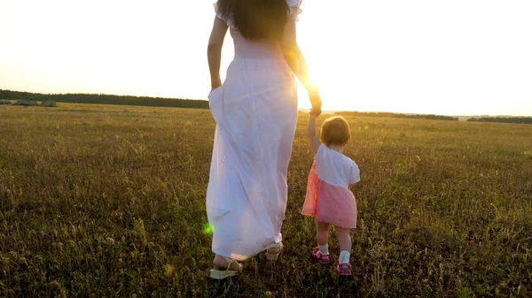 Petit bébé va de l'avant tenant sa main de mère dans le coucher de soleil lumineux — Photo