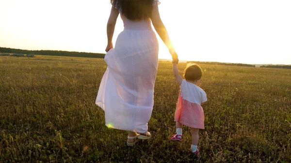 Petit bébé va de l'avant tenant sa main de mère dans le coucher de soleil lumineux — Photo