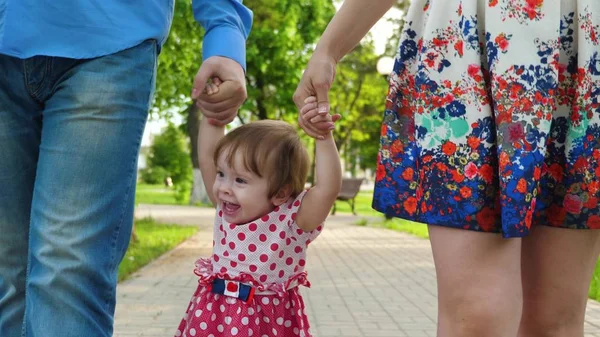 Mamá y papá juegan con el bebé crían al bebé con las manos arriba, niña saltando y riendo, caminata familiar en el parque en verano — Foto de Stock