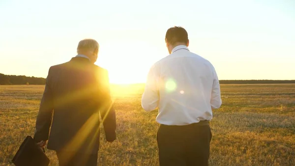 Een oudere zakenman in ernstige pak met werkmap in zijn hand geeft werkplan aan de medewerker van het bedrijf in de avond in heldere ondergaande zon — Stockfoto