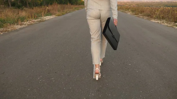 Obchodní žena s černou aktovkou kráčí ve světle obleku a bílé boty s vysokými podpatky jsou procházky po asfaltu s odznaky, pohled zezadu — Stock fotografie