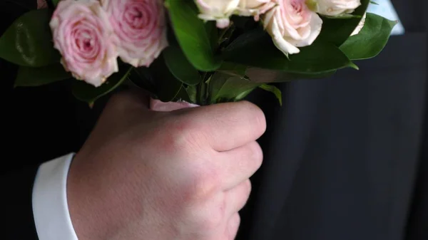 Mazzo di rose multicolori in mani di uomo in un vestito scuro e camicia bianca. primo piano — Foto Stock