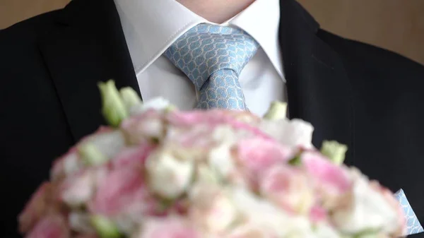 Μπουκέτο με πολύχρωμα τριαντάφυλλα στα χέρια του ανθρώπου σε ένα σκούρο κοστούμι και άσπρο πουκάμισο. γκρο πλαν — Φωτογραφία Αρχείου