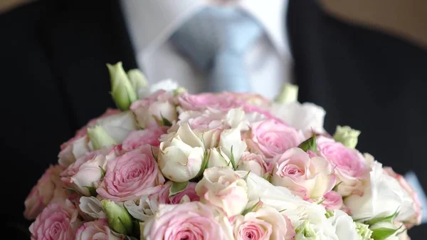 Μπουκέτο με πολύχρωμα τριαντάφυλλα στα χέρια του ανθρώπου σε ένα σκούρο κοστούμι και άσπρο πουκάμισο. γκρο πλαν — Φωτογραφία Αρχείου