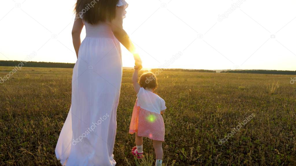 Little baby goes forward holding his mom hand in bright sunset