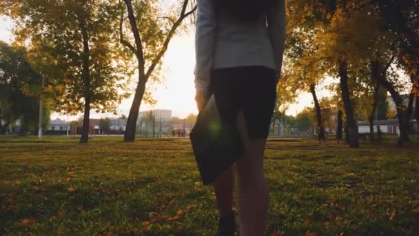 Mujer de negocios con maletín de documentos cae en el césped en el parque en el resplandor de la puesta del sol. Primer plano de las piernas — Vídeo de stock