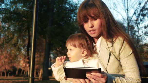 엄마와 아이 태블릿에 책을 읽고 공원 벤치에 앉아 있다. — 비디오