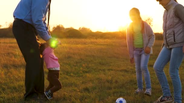 Папа играет с детьми в футбол на поле и улыбается. Семейный отдых вечером после тяжелого рабочего дня. Девочки играют с младшей сестрой — стоковое видео
