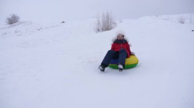 Kız, kışın karda yüksek tepe kızak ve bir şişme kar tüp üzerinde slaytlar. Genç kız bir kış parkta Noel tatili üzerinde çalış. Ağır çekim.