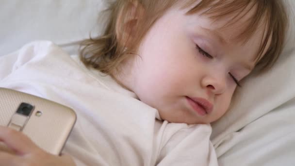 Kleine baby sliep op kussen met telefoon in zijn hand. Kind slaapt in bed met smartphone in zijn hand — Stockvideo