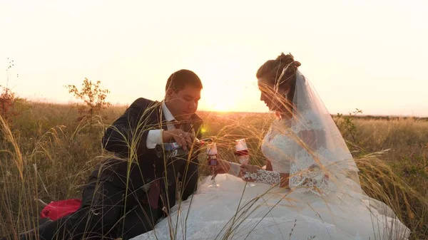 Ženich nalévá lahodné sklenic vína v oblasti světlé paprsky slunce pro nevěstu. šťastní novomanželé pijí šampaňské na louce v paprscích krásný západ slunce. koncept šťastný svatba — Stock fotografie