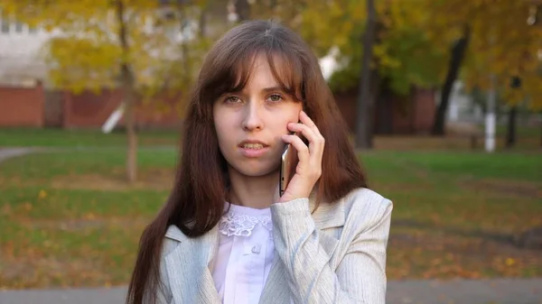 Krásná žena mluví o smartphone a usmívá se. dívka je mluvit na mobilním telefonu a procházky večer v městském parku — Stock fotografie