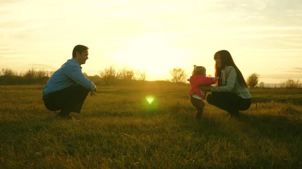 Baby geht auf Rasen von Papa zu Mama. Kind macht erste Schritte im Park Mama und Papa spielen mit Kindern auf dem Rasen bei Sonnenuntergang. Familienglück — Stockfoto