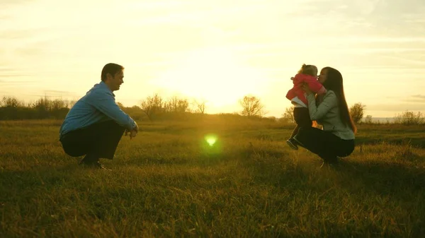 Baby geht auf Rasen von Papa zu Mama. Kind macht erste Schritte im Park Mama und Papa spielen mit Kindern auf dem Rasen bei Sonnenuntergang. Familienglück — Stockfoto