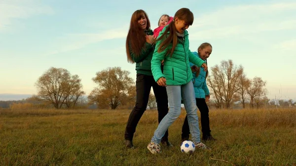 Papá patea la pelota de fútbol. niños y mamá juegan al fútbol en el campo. Familia jugando con un niño pequeño por la pelota de los niños en un parque. Movimiento lento . — Foto de Stock