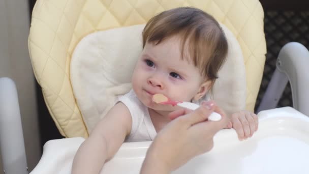 Малыш учится есть кашу из ложки. Мама впервые вводит ребенка в диету — стоковое видео