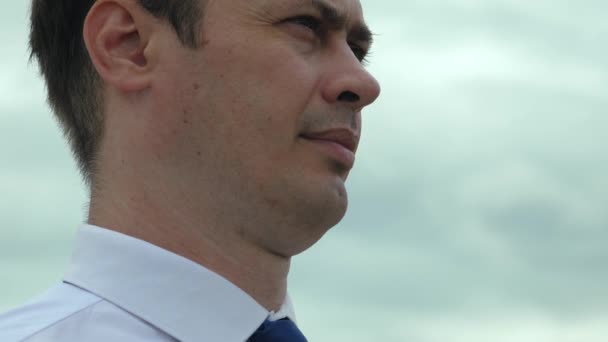 Un hombre serio adulto con camisa blanca mira a la distancia contra el fondo del sombrío cielo gris. Primer plano — Vídeos de Stock