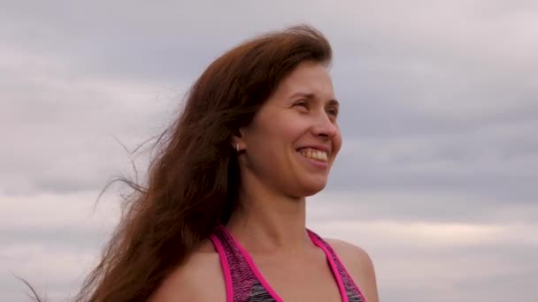 Chica con el desarrollo de pelo largo está sonriendo contra el cielo oscuro. La mujer camina con el tiempo nublado por la noche. Primer plano — Vídeos de Stock