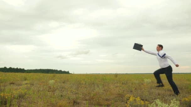 Ein fröhlicher Geschäftsmann in weißem Hemd und Krawatte läuft mit Aktentasche in der Hand über das Feld und lächelt. Mann freut sich über perfekten Deal — Stockvideo