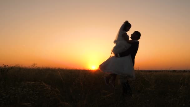 El hombre está dando vueltas a su esposa al atardecer. Familia joven enamorada en luna de miel — Vídeos de Stock