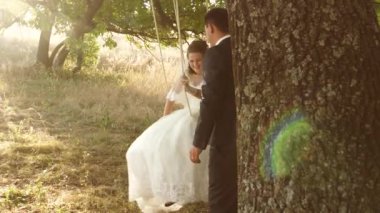 Damat gelini salıncak ve sevgi dolu bakışla gülümsüyor sallıyor. Kadın ve adam romantik toplantıda günbatımı önemli mutluyuz