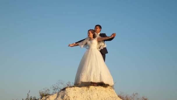 Ευτυχισμένη νύφη και τον γαμπρό αγκαλιά και ανεβαίνουν ενώ ισιώνει τα χέρια τους ενάντια σε γαλάζιο καθαρό ουρανό και να χαμογελά. Ρομαντικό ταξίδι για ζευγάρια. Ταξιδεύουν ζευγάρια — Αρχείο Βίντεο