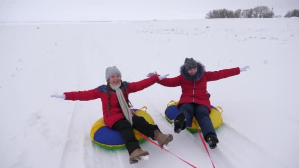 Девушки идут на снежную тарелку по белой снежной дороге и с удовольствием смеются. Зимнее веселье веселые подростки в морозный день — стоковое видео