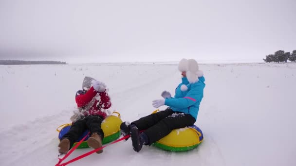 Funny mothers and their daughter are riding snowy plate along snowy winter road, laughing and playing snowballs. Family life as way of life. Girls laugh, play snowballs and ride on sled — Stock Video