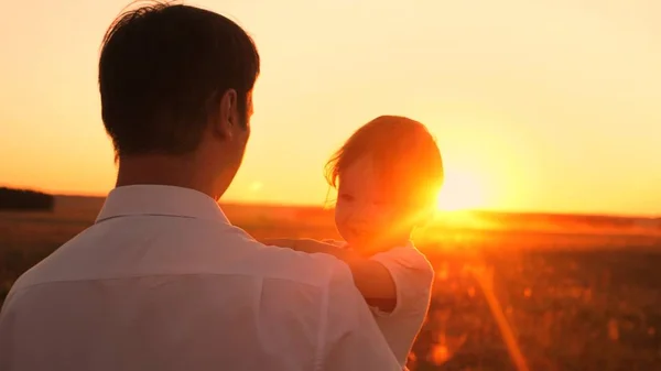 Gelukkig Papa en dochtertje in haar armen op zonsondergang felle zon zitten. Meisje lacht spelen met papa op avond wandeling. Close-up — Stockfoto