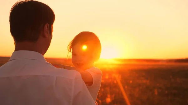 Joyeux papa et petite fille assis dans ses bras au coucher du soleil soleil. Fille rit en jouant avec papa sur la promenade du soir. Gros plan — Photo