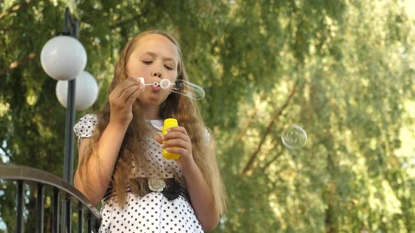 Mädchen bläst Seifenblasen auf und lächelt im Sommerpark. — Stockfoto