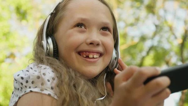 Šťastná dívka se sluchátky s telefonem poslouchá hudbu a usmíval se tančí v městě letní. — Stock fotografie