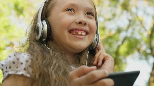 Glückliches Mädchen mit Kopfhörern und Telefon, das Musik hört und lächelnd in einer Sommerstadt tanzt. — Stockfoto