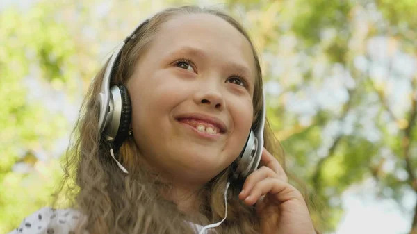 Glückliches Mädchen mit Kopfhörern und Telefon, das Musik hört und lächelnd in einer Sommerstadt tanzt. — Stockfoto