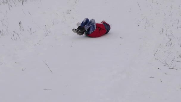 Vidám gyermek a piros kabát diák szán a hóban egy magas hegy és nevet. boldog lány játék karácsonyi ünnep a téli park. Lassú mozgás — Stock videók