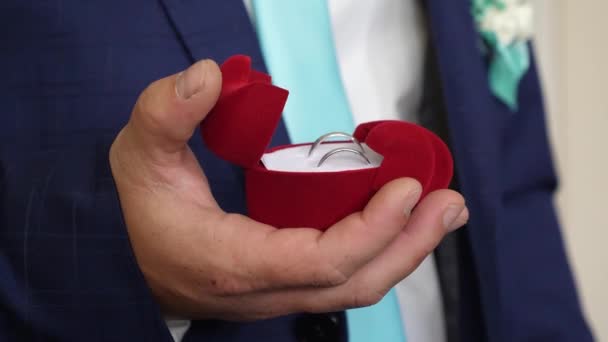 El novio sostiene la caja con anillos de boda en su mano para su propuesta a su amada. Crear una nueva familia. Primer plano — Vídeos de Stock