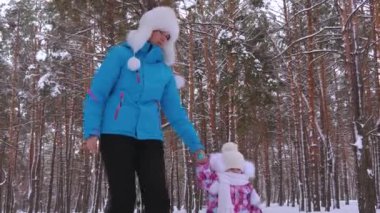 Nanny leads hand of little girl on snowy road while walking in fresh air in park in winter. Mom and daughter make first steps in winter forest