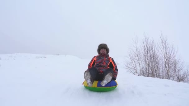 Man glider ner snöiga berg på snö tefat och skrattar. Jullov på kälke på vintern — Stockvideo