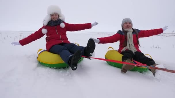 Счастливые дети катаются на снежной горе, выпрямляют руки в полете и смеются. Счастливого детства зимой на санях. Рождественские каникулы — стоковое видео