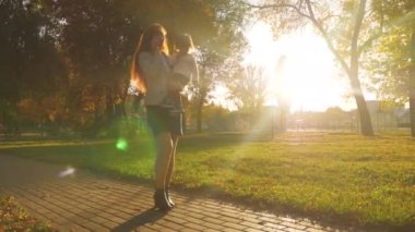 Mutlu anne ve bebek Park'ta sıcak akşam üzerinde yürüyor. İş kadını iş takım küçük bebek ile smartphone üzerinde konuşmak ve gün batımı ışık sonbahar parkta yürüyüş.