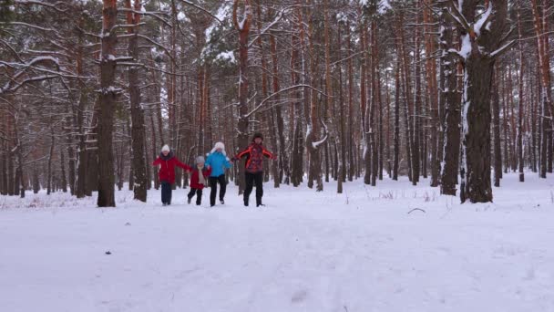 Щасливі батьки і діти бігають по засніженій зимовій дорозі в хвойному парку і сміються в зимовий морозний день. Сімейні ігри на свіжому повітрі. Малюк посміхається батькам. Різдвяні свята — стокове відео