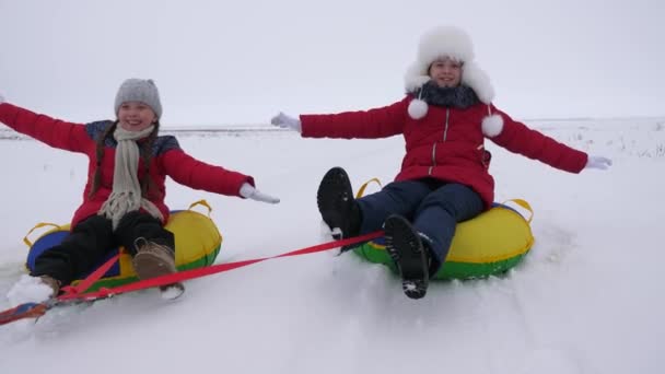 Happy children have fun riding snow saucer and laugh on snowy winter road on winter frosty day. Teens play on sled in winter field and smile. Games in fresh frosty air. Christmas Holidays — ストック動画
