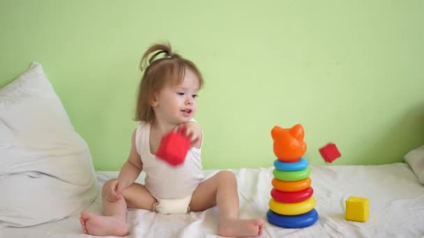 Criança está se recuperando em instalações médicas, sentado na cama e brincando em cubos macios coloridos e pirâmide e sorrisos. Recuperação de criança na enfermaria do hospital — Vídeo de Stock