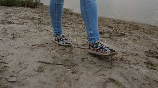 Flickor ben i jeans och skor gå till stranden, flicka går till sjön i kväll — Stockfoto