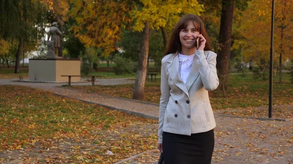 Schöne Geschäftsfrau, die mit dem Handy spricht, glückliche Frau, die durch den herbstlichen Park geht und lächelt — Stockfoto